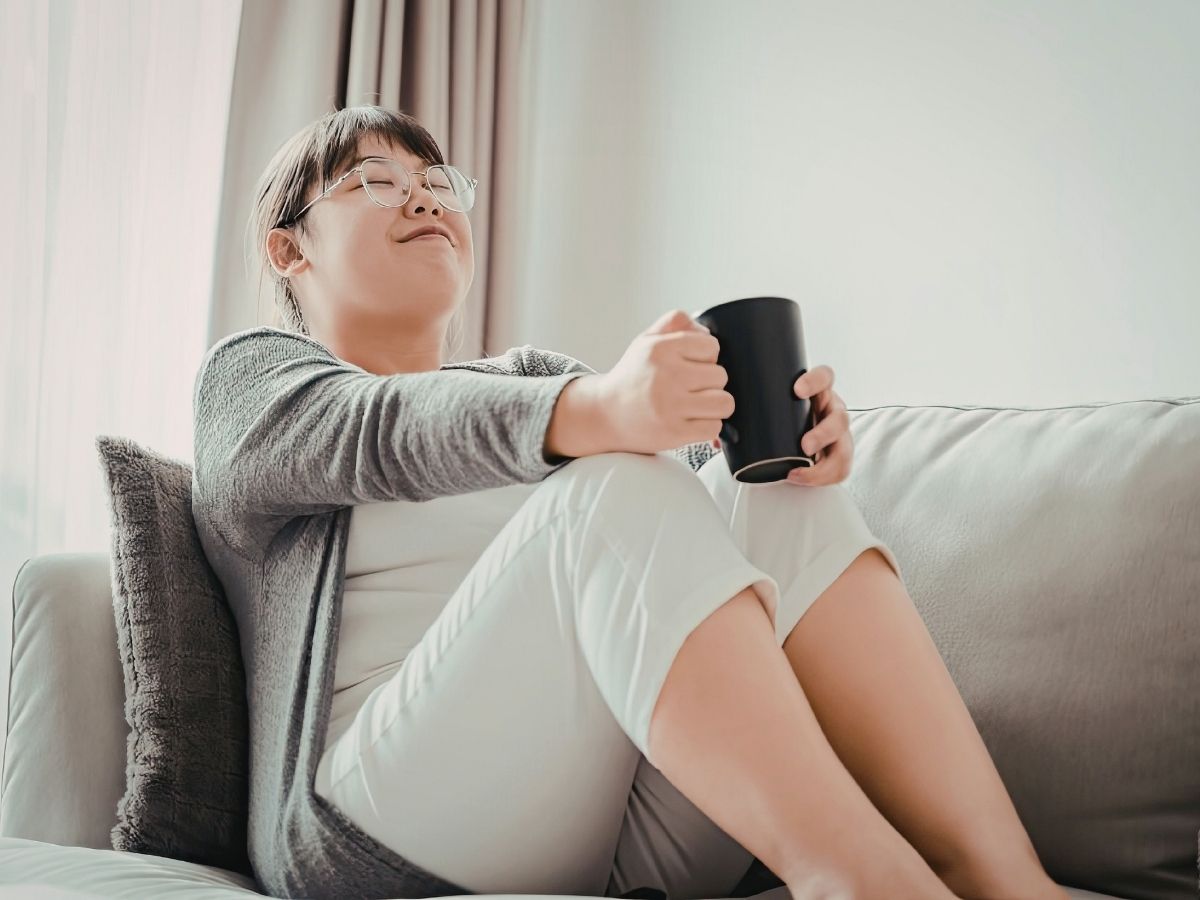 一位坐在沙發上拿著杯子休息的亞洲女性，象徵在壓力與焦慮中慢下來